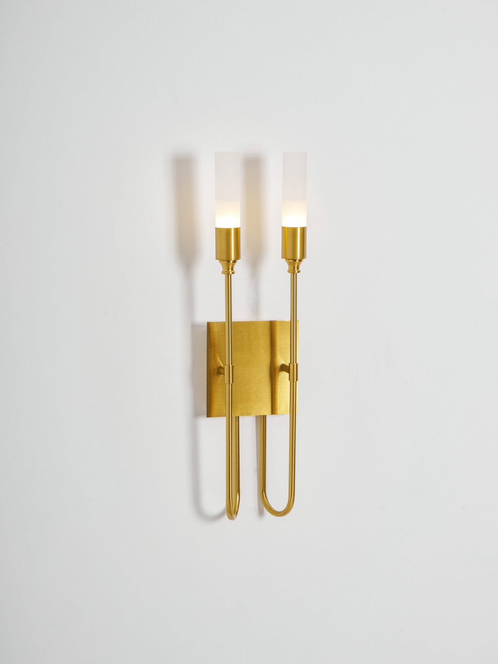Smaller view of this lit brass Clérachic two-light sconce on a pale grey wall, with plenty of empty space around it.