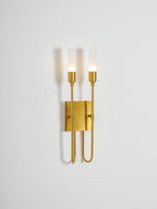 Smaller view of this lit brass Clérachic two-light sconce on a pale grey wall, with plenty of empty space around it.