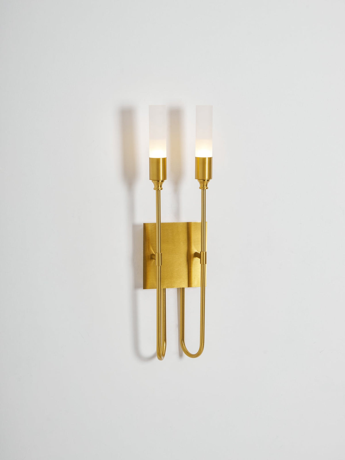 Smaller view of this lit brass Clérachic two-light sconce on a pale grey wall, with plenty of empty space around it.