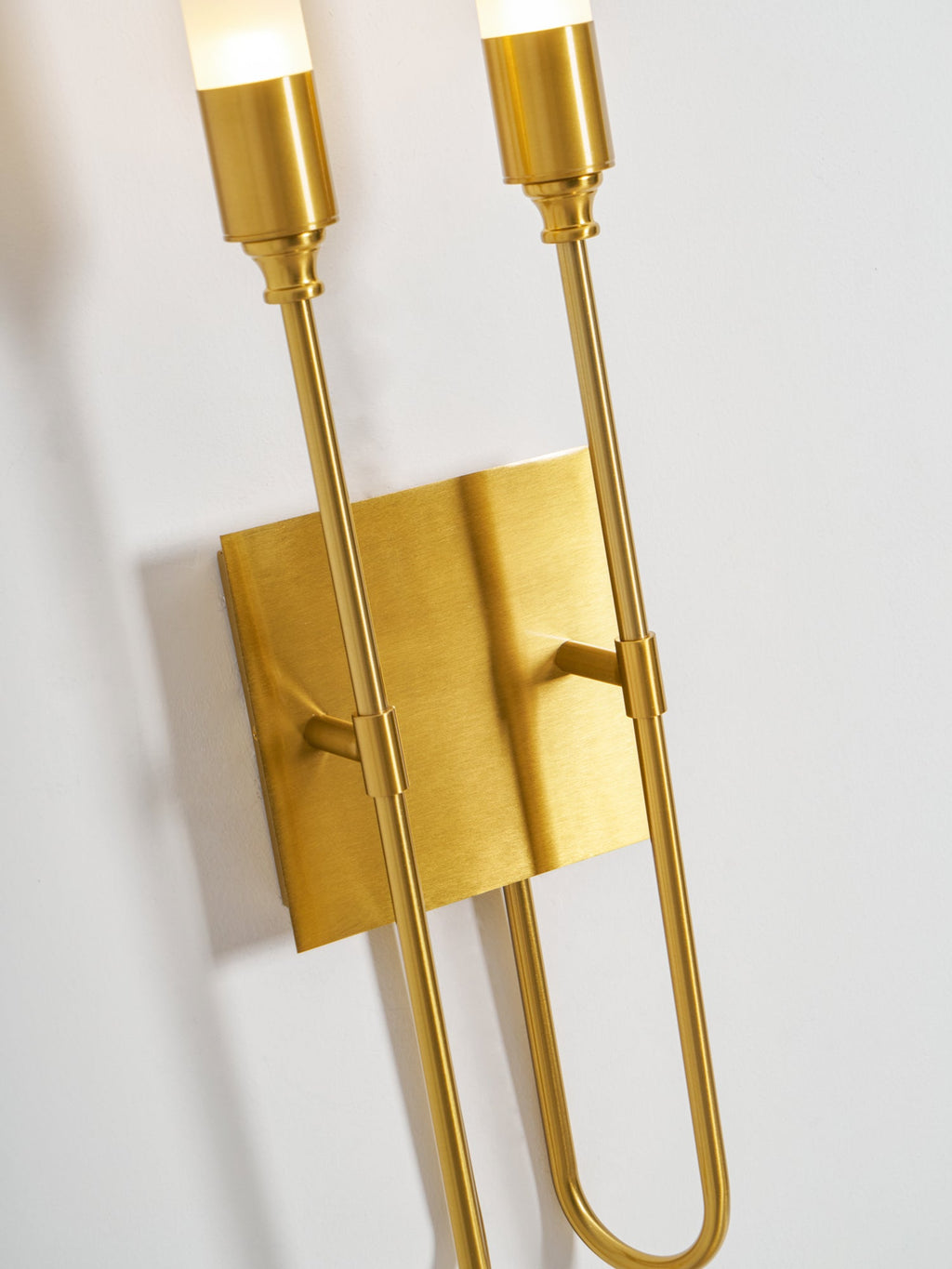 Close, angled view of the brass collars, plate and looped arms of this Clérachic two-light sconce.