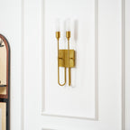 Close view of a brass two-light Clérachic sconce on a white panelled wall, the arched cabinet edge showing at the left.