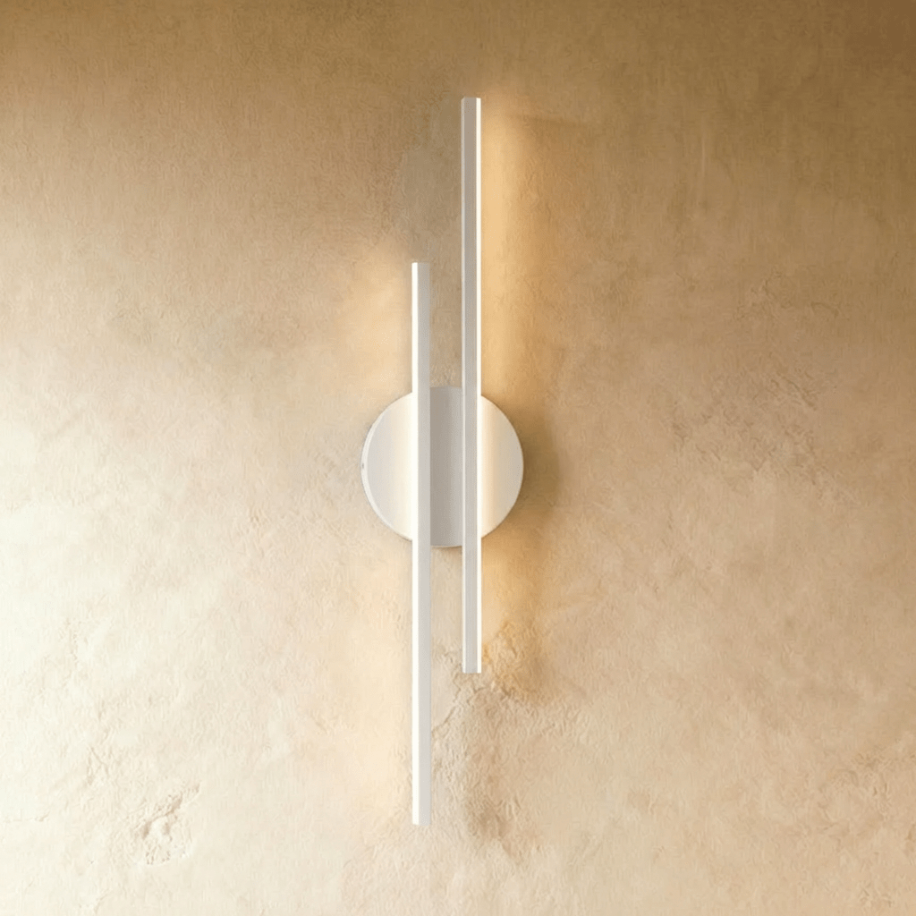 Clérachic wall light with two slim white light bars of different lengths on a round white backplate, glowing on plaster