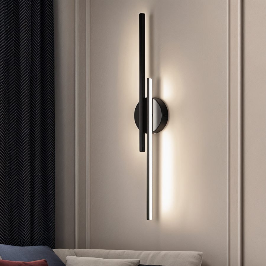 Clérachic black two-bar wall light with a glowing white tube, mounted on a panelled wall above a sofa and dark herringbone curtain