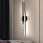 Clérachic black two-bar wall light with a glowing white tube, mounted on a panelled wall above a sofa and dark herringbone curtain