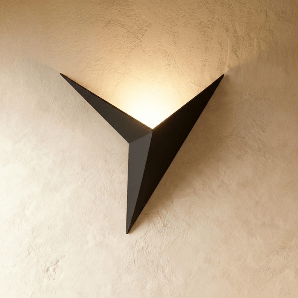 A Clérachic slim iron wall sconce in matte black casts a warm upward glow across a plaster wall corner.