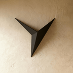 The Clérachic slim iron wall sconce in matte black shown unlit, its angular triangular form against a plaster wall.