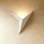 A Clérachic slim iron wall sconce in matte white casts a warm upward glow across a plaster wall corner.