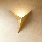 A Clérachic slim iron wall sconce in brushed gold casts a warm upward glow across a plaster wall corner.
