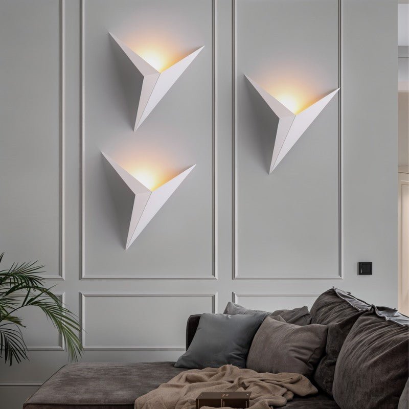 Three Clérachic slim iron wall sconces in matte white cast a warm glow above a sofa in a paneled living room.