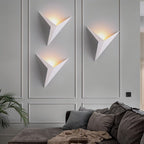 Three Clérachic slim iron wall sconces in matte white cast a warm glow above a sofa in a paneled living room.