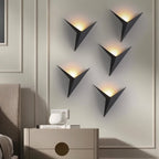 Five Clérachic slim iron wall sconces in matte black light a bedroom wall in a staggered pattern above a nightstand.