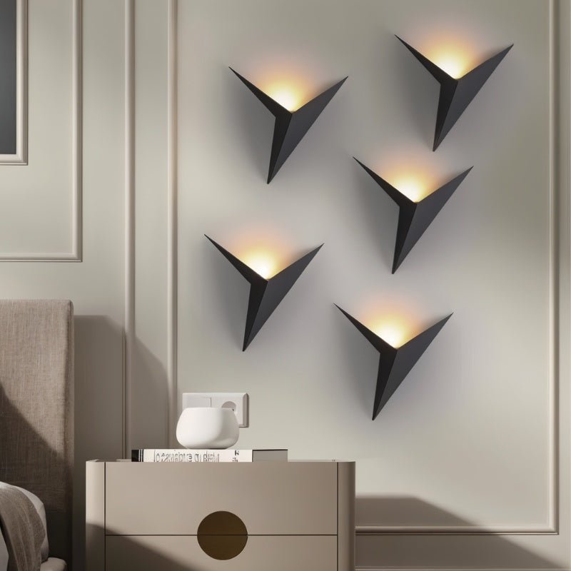 Five Clérachic slim iron wall sconces in matte black light a bedroom wall in a staggered pattern above a nightstand.
