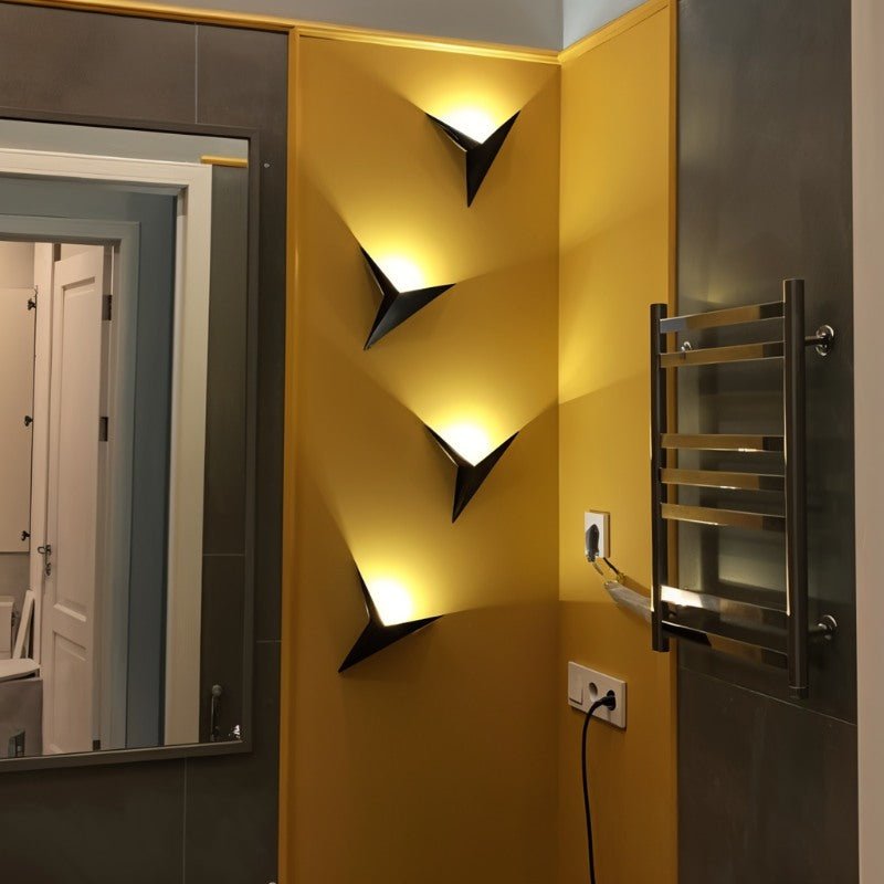 Four Clérachic slim iron wall sconces in matte black stack down a mustard accent wall beside a bathroom mirror.