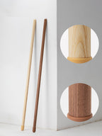Light wood and walnut-colour Clérachic floor lamps leaning together on a white wall, with round insets of each foot.