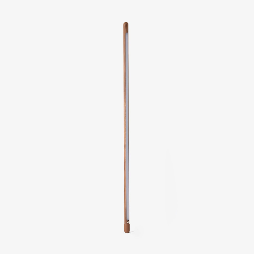 Walnut-colour Clérachic floor lamp standing upright with its frosted strip facing out, on a plain light backdrop.