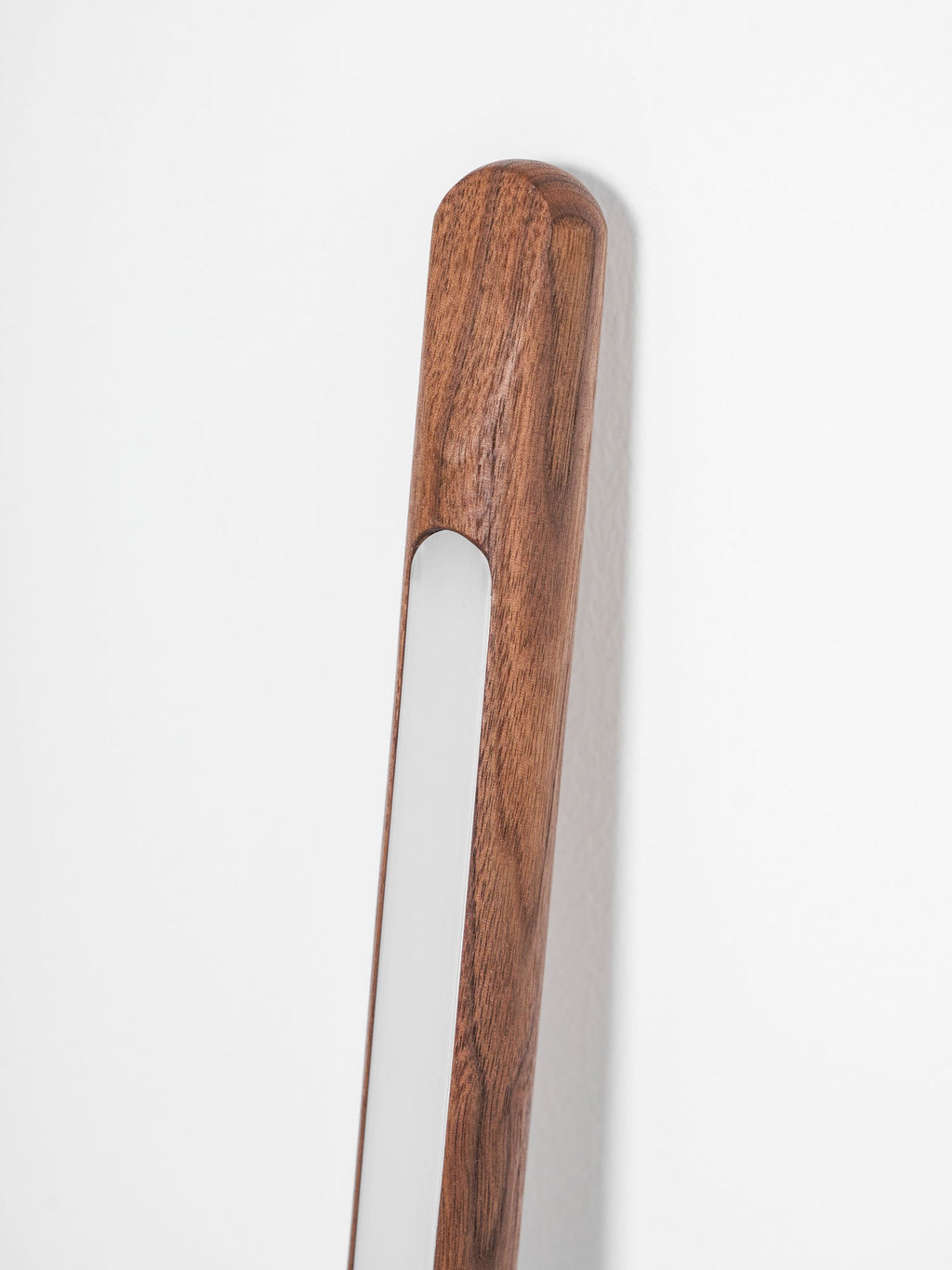 Top end of this Clérachic walnut-colour floor lamp, leaning on a white wall, with its frosted light strip beside the grain.