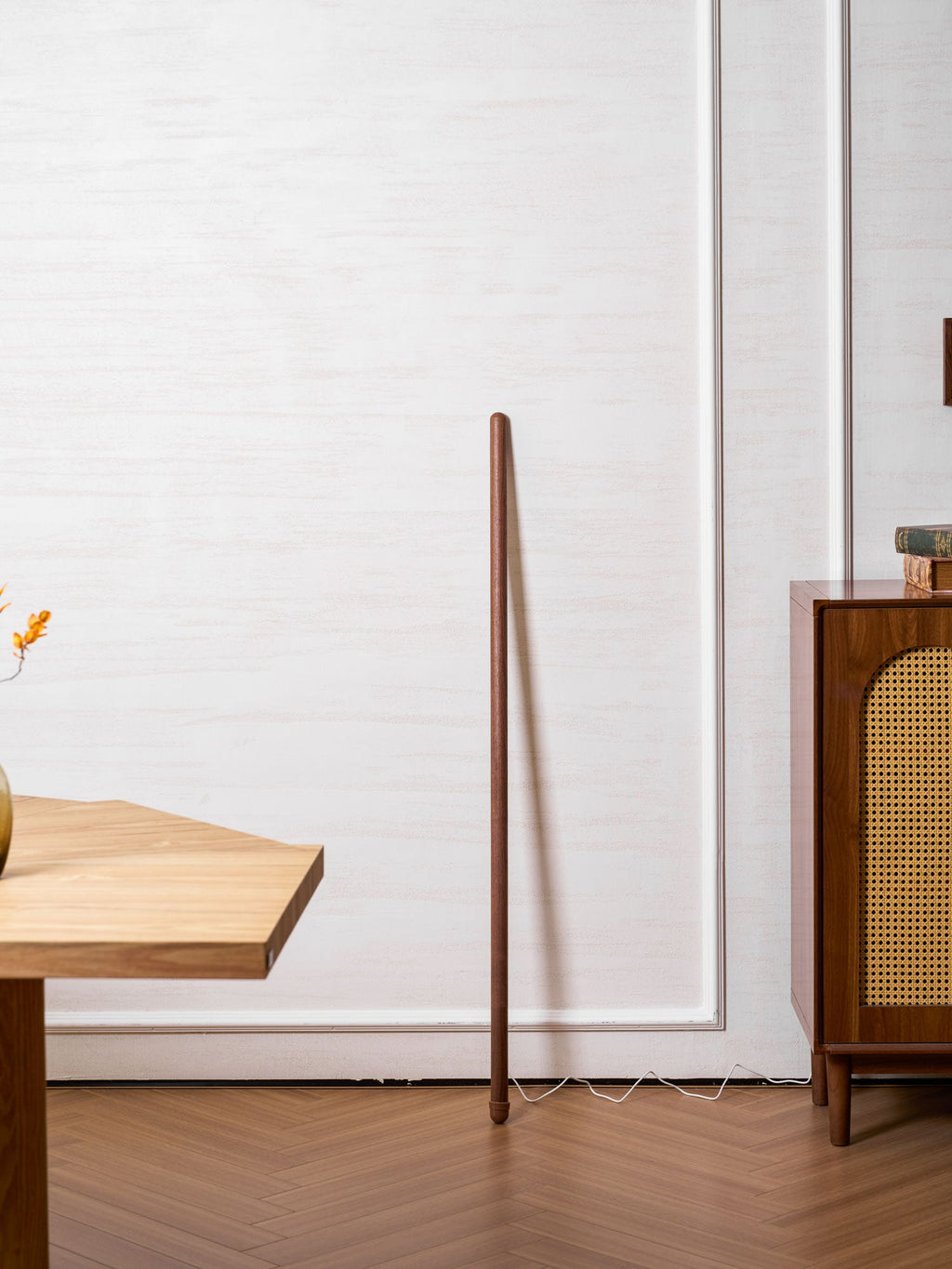 Walnut-colour Clérachic floor lamp, switched off, leaning near a wooden table edge on a herringbone floor.