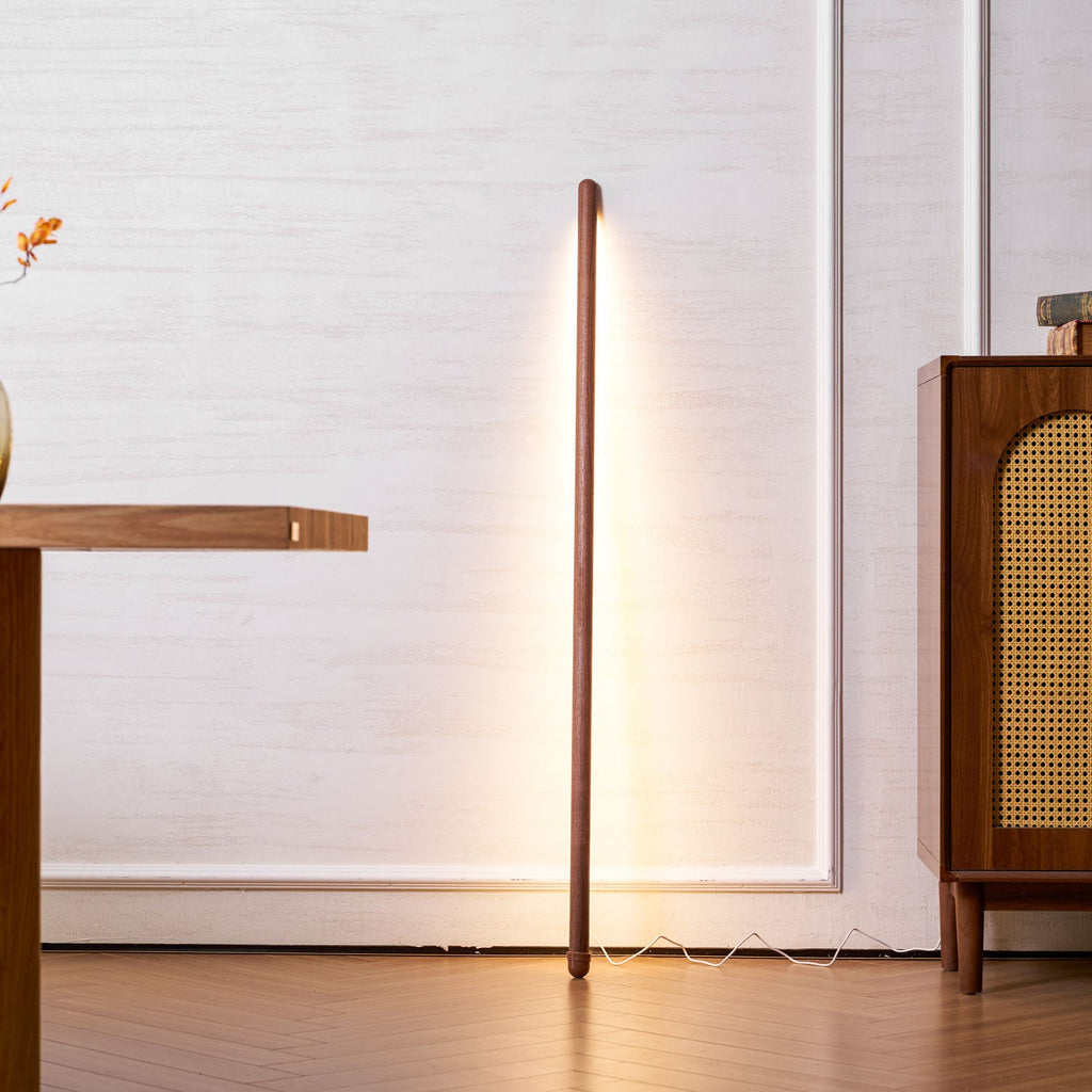 Clérachic floor lamp glowing warm in walnut colour beside a wooden desk and a rattan-fronted cabinet.