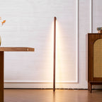 Clérachic floor lamp glowing warm in walnut colour beside a wooden desk and a rattan-fronted cabinet.