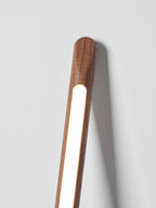 Close view of the top of this Clérachic walnut-colour floor lamp glowing warm against a pale grey wall.