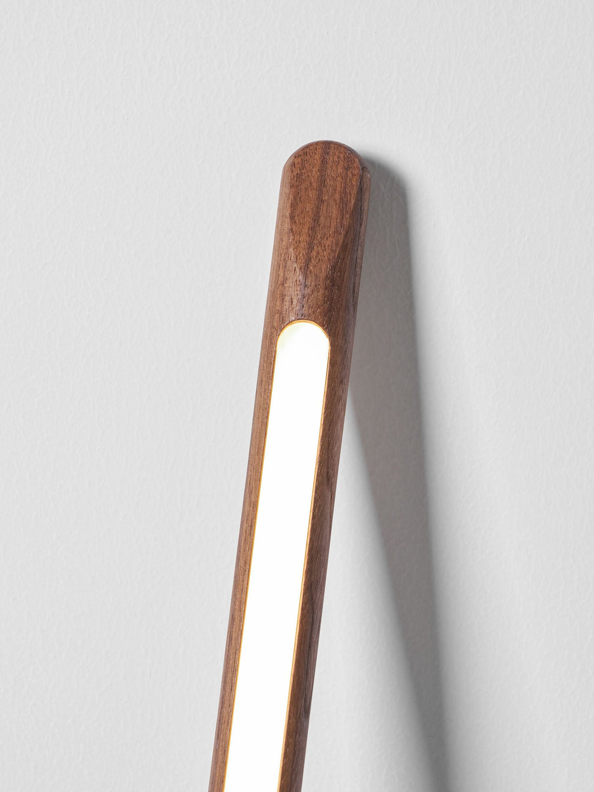 Close view of the top of this Clérachic walnut-colour floor lamp glowing warm against a pale grey wall.