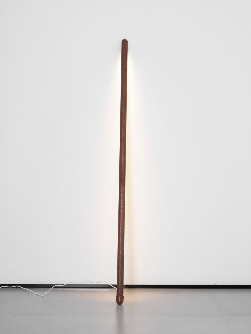 Slim walnut-colour Clérachic floor lamp upright against a pale wall, its light strip casting a soft line of light.