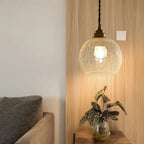 Clérachic crackle-glass globe pendant with a brass lamp holder, hung beside a timber panel above a side table.