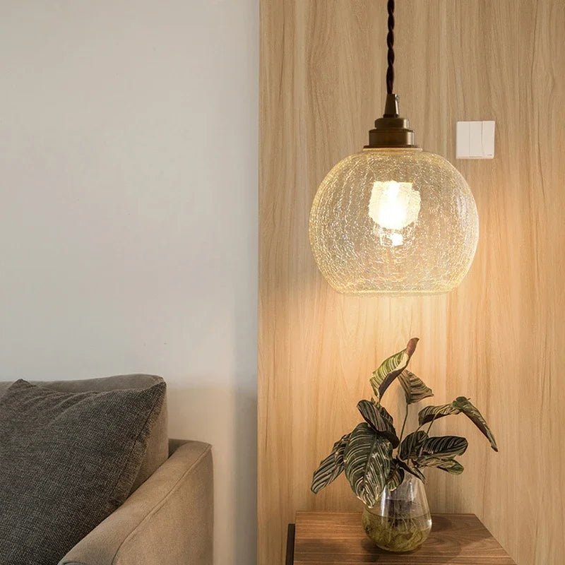 Clérachic crackle-glass globe pendant with a brass lamp holder, hung beside a timber panel above a side table.