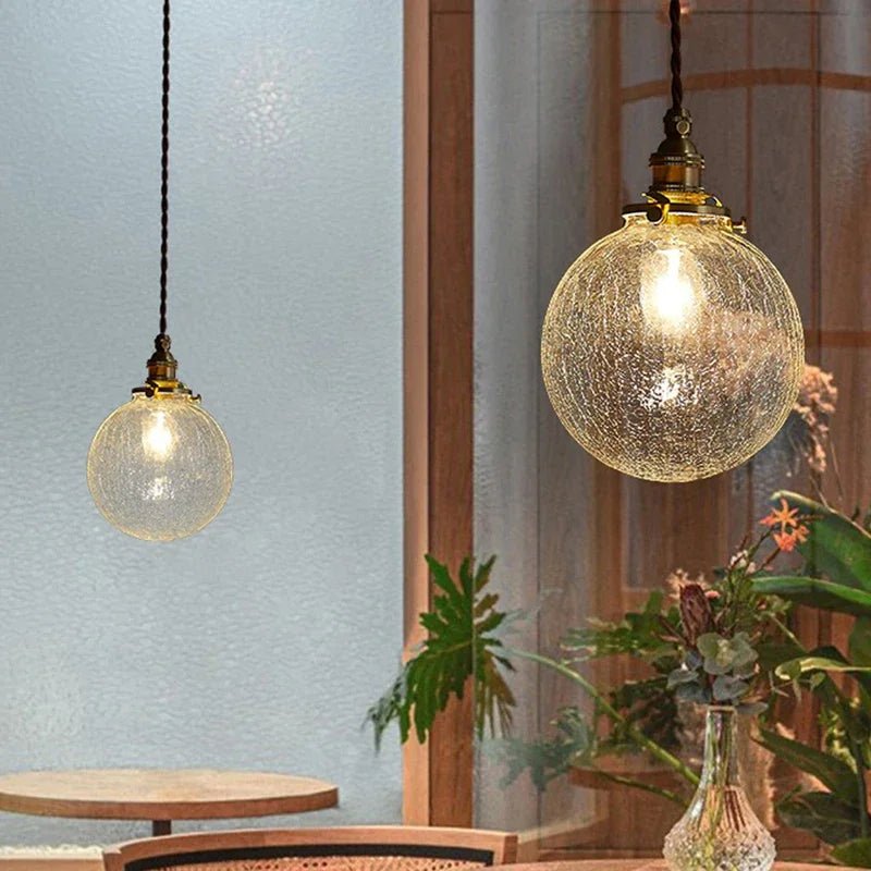 Two Clérachic crackle-glass globe pendants in different sizes hung on twisted cords beside a window and plants.
