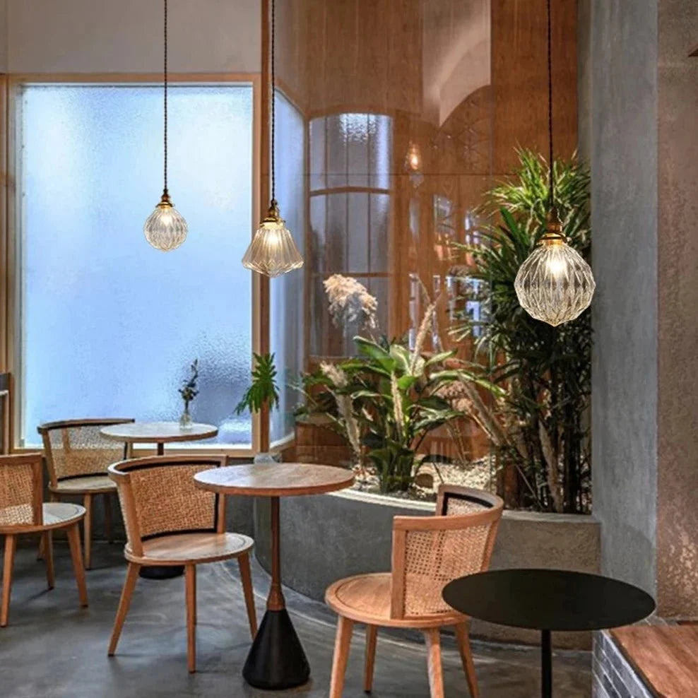 Three Clérachic ribbed and faceted glass pendants with brass holders hung above café tables and cane chairs.