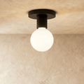 Clérachic compact black ceiling light with a round canopy, short cylinder and a frosted white globe bulb on limewash.