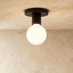 Clérachic compact black ceiling light with a round canopy, short cylinder and a frosted white globe bulb on limewash.