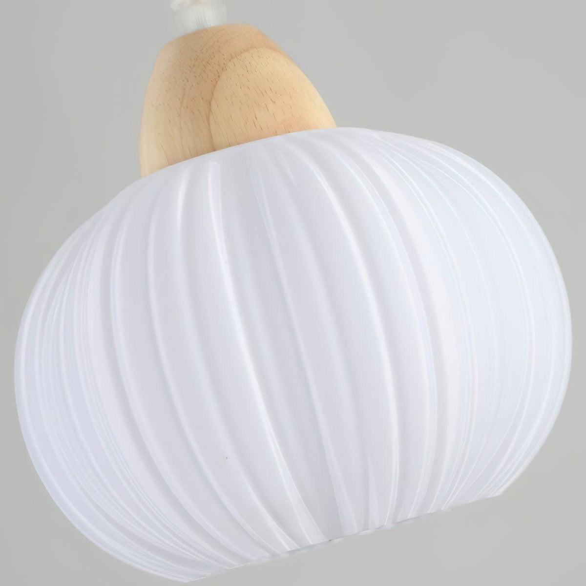 Clérachic fluted pendant lamp seen from below and to one side, the vertical ribbing of the white acrylic curving away from the wood cap.