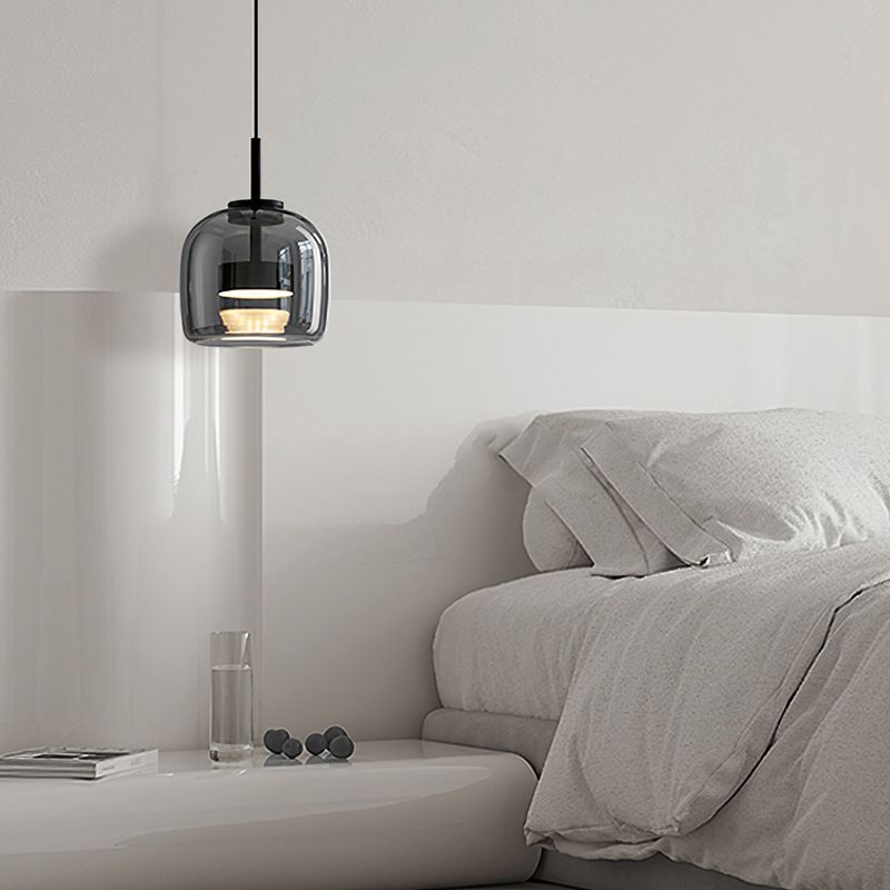 Clérachic smoke gray glass dome pendant lit low over a pale bedside table beside a linen-dressed bed.
