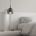 Clérachic smoke gray glass dome pendant lit low over a pale bedside table beside a linen-dressed bed.