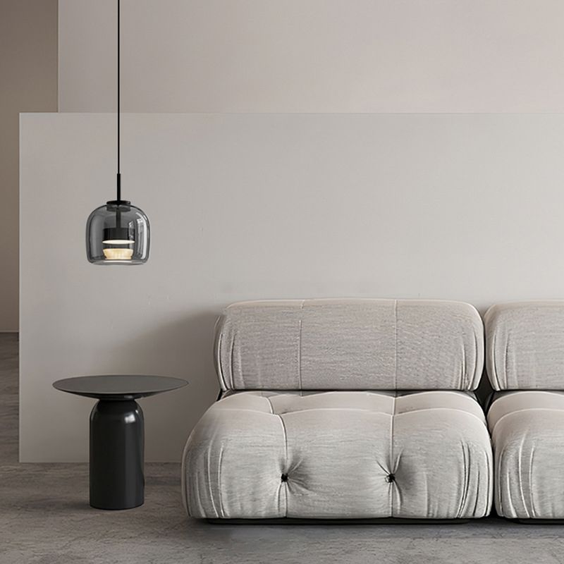 The Clérachic smoke gray glass dome pendant hangs beside a tufted cream sofa, its warm ring glowing above a black side table.