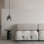 The Clérachic smoke gray glass dome pendant hangs beside a tufted cream sofa, its warm ring glowing above a black side table.
