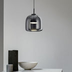 Clérachic smoke gray glass dome pendant seen close over a console, the tinted glass showing the twin frosted discs inside.