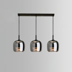 Studio view of the Clérachic pendant in its 3-head linear bar version, three smoke gray domes lit warm beneath a black bar canopy.