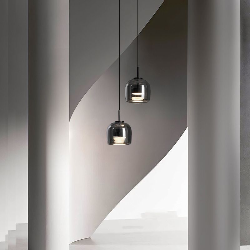 Two Clérachic smoke gray pendants staggered in a sculptural white stairwell, reading almost mirror-dark against the curved plaster.