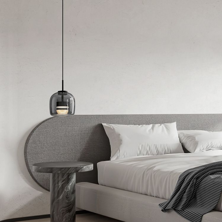 Clérachic smoke gray glass pendant on a long cord beside an upholstered headboard, standing in for a bedside lamp and freeing the table.