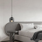 Clérachic smoke gray glass pendant on a long cord beside an upholstered headboard, standing in for a bedside lamp and freeing the table.
