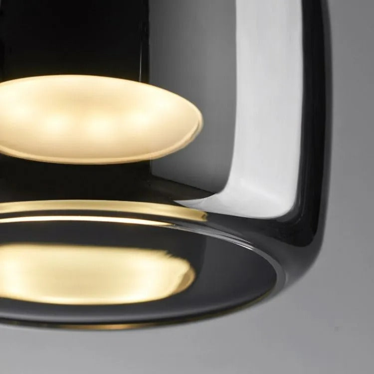 Macro detail of the Clérachic pendant's two lit diffuser discs glowing amber behind the tinted smoke gray glass.