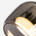 Angled close-up of the Clérachic pendant's smoke gray glass rim with the warm diffuser glowing just inside it.