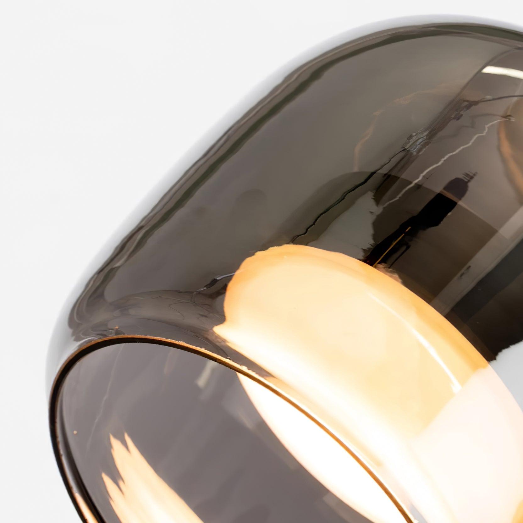 Angled close-up of the Clérachic pendant's smoke gray glass rim with the warm diffuser glowing just inside it.