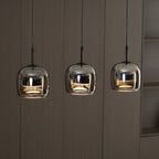 Three Clérachic smoke gray pendants lit in a row against pale wood panelling, each dome mirroring the room around it.