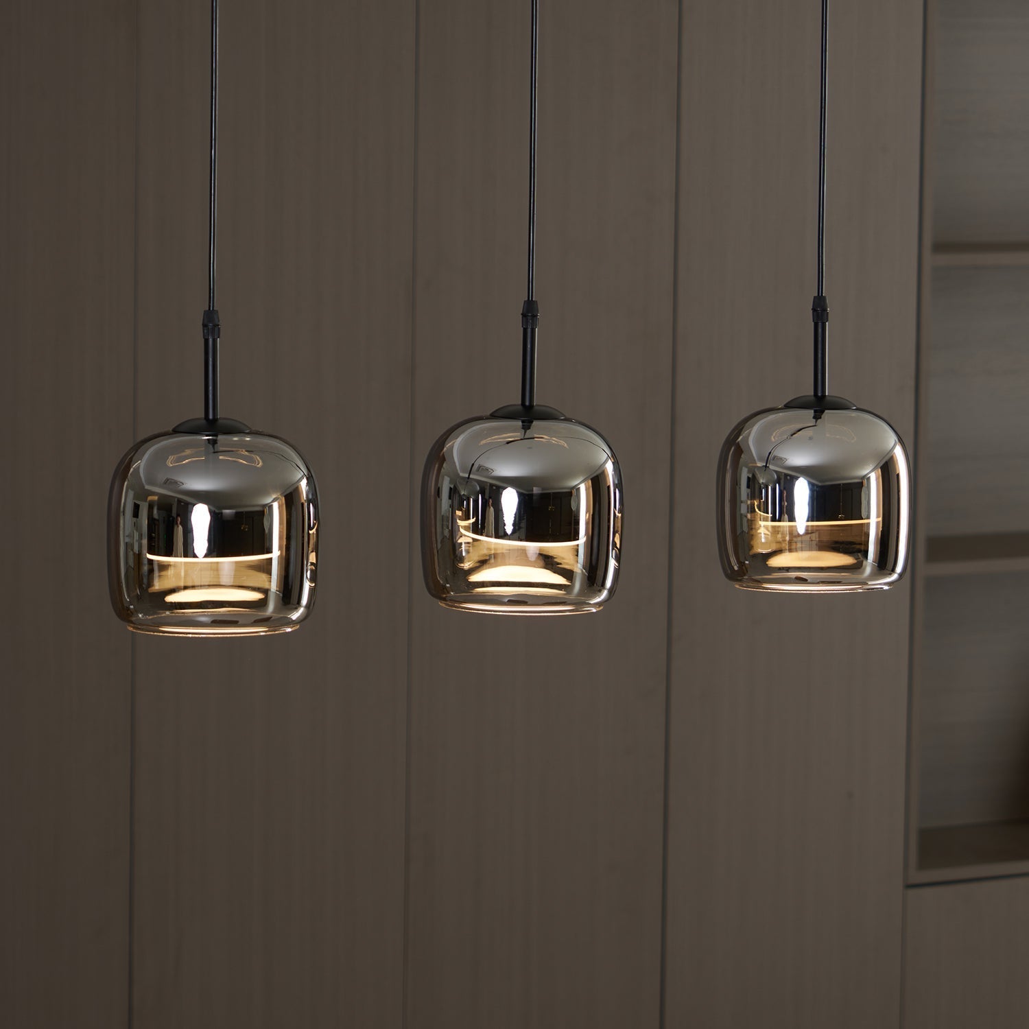 Three Clérachic smoke gray pendants lit in a row against pale wood panelling, each dome mirroring the room around it.