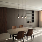 Clérachic smoke gray pendants in a row of three over a stone dining table, lit in a sunlit room with tan leather chairs.