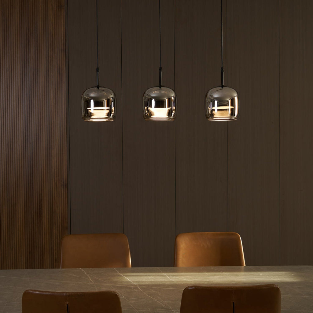 After dark, three Clérachic smoke gray pendants pool warm light onto a stone dining table set against dark wood panelling.