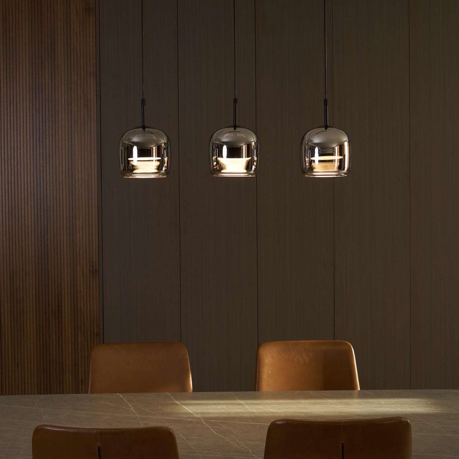 After dark, three Clérachic smoke gray pendants pool warm light onto a stone dining table set against dark wood panelling.